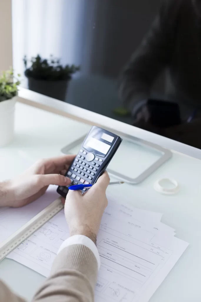Manos utilizando una calculadora junto a un computador.