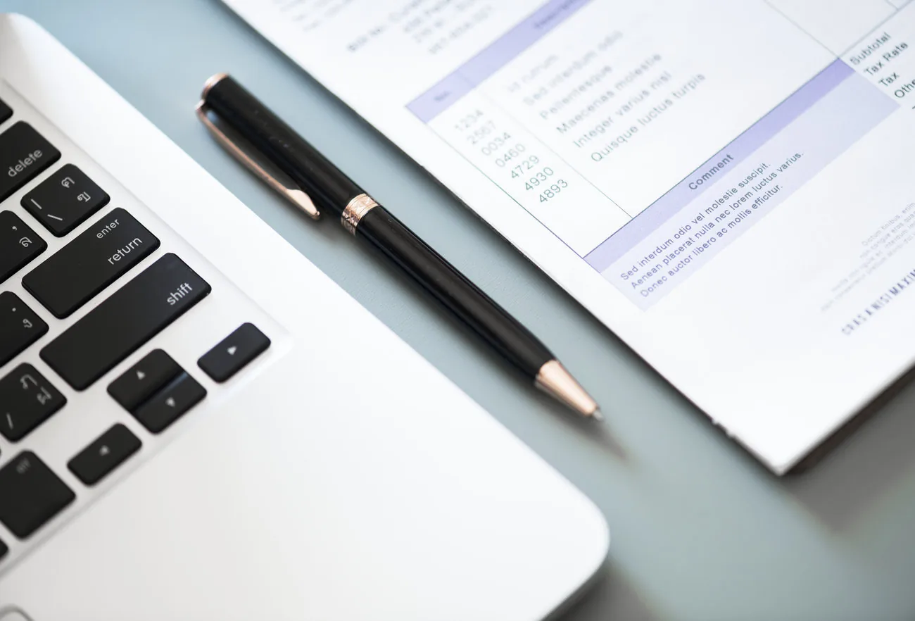 Computador portátil y documentos financieros sobre una mesa de trabajo.