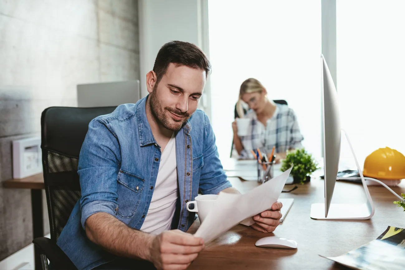 Profesional revisando documentos y trabajando en un computador portátil.