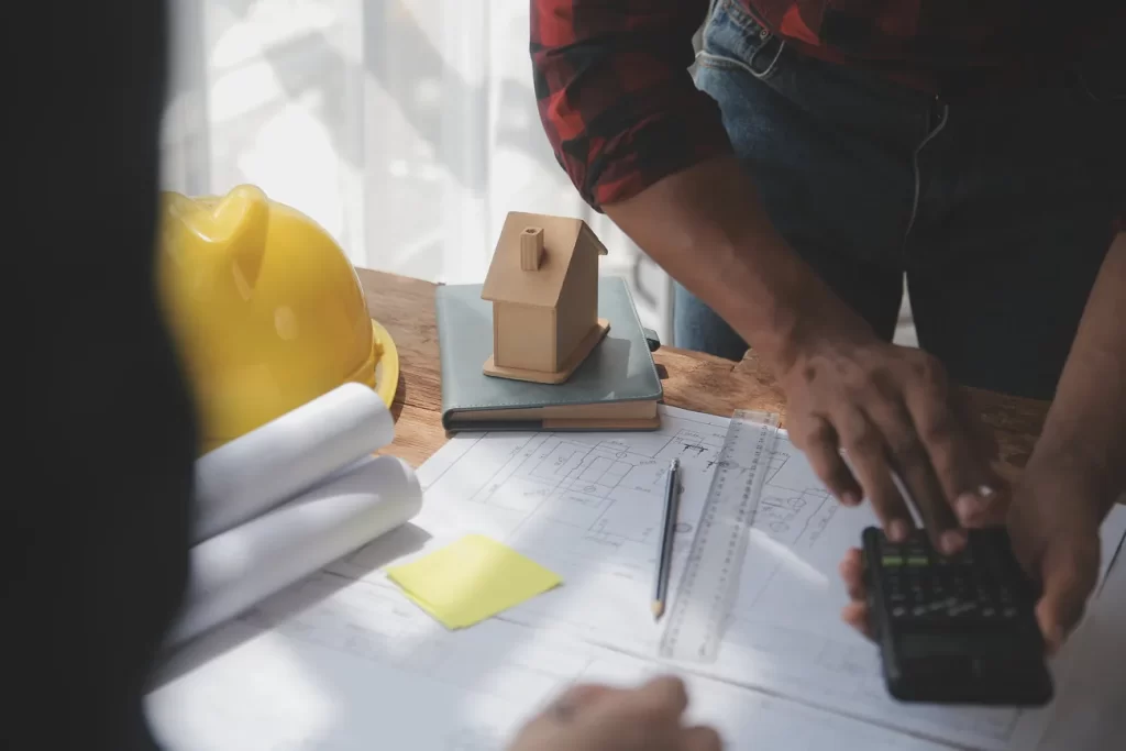 Profesional de construcción revisando planos y cálculos en una mesa de trabajo.