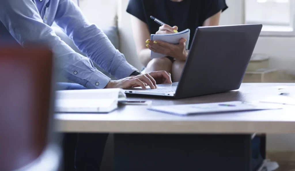 Dos profesionales comparando información en documentos y computador.